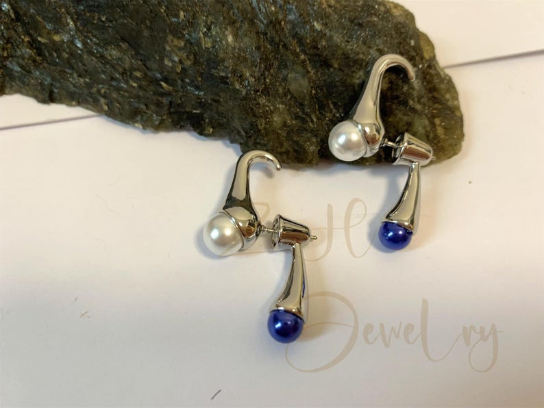 May include: A pair of silver earrings with a white pearl on one side and a blue pearl on the other side.