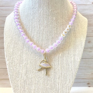 May include: A purple and clear beaded necklace with a gold ballerina charm and white beads spelling "ELLA".