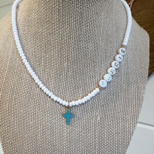 May include: White beaded necklace with a gold cross charm and the name "GRACE" spelled out in gold letters on the beads.