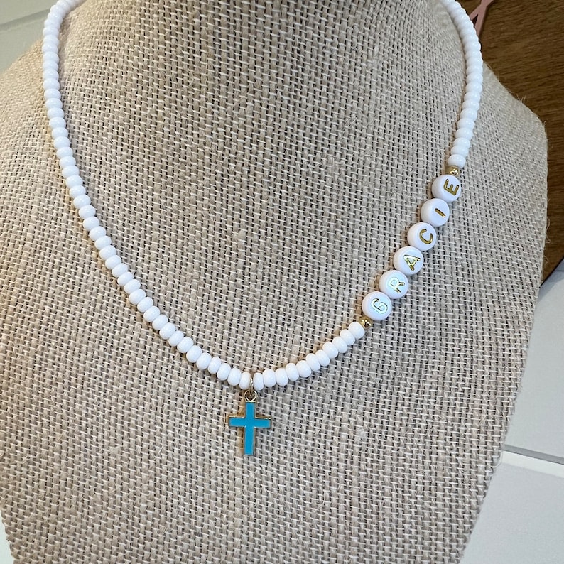 May include: White beaded necklace with a gold cross charm and the name "GRACE" spelled out in gold letters on the beads.