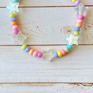 May include: A rainbow-colored beaded bracelet with clear star-shaped charms. The bracelet is made with pastel pink, yellow, blue, and purple beads.