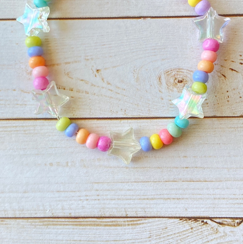 May include: A rainbow-colored beaded bracelet with clear star-shaped charms. The bracelet is made with pastel pink, yellow, blue, and purple beads.