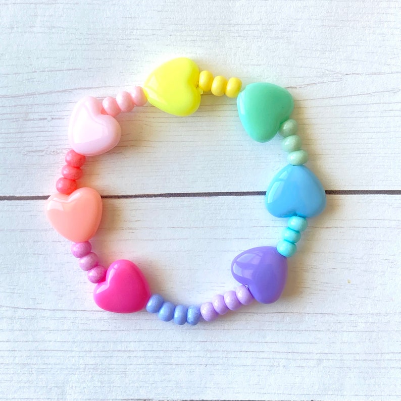 May include: A rainbow heart bracelet with pastel pink, orange, yellow, green, blue, and purple heart beads. The bracelet is made with small round beads in between the heart beads.