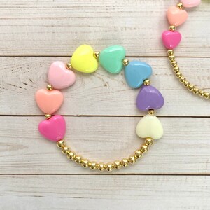 Puede incluir: Un brazalete de cadena dorada con cuentas de coraz&oacute;n en forma de coraz&oacute;n pastel en un patr&oacute;n de arco&iacute;ris.