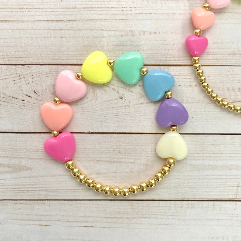 Puede incluir: Un brazalete de cadena dorada con cuentas de coraz&oacute;n en forma de coraz&oacute;n pastel en un patr&oacute;n de arco&iacute;ris.