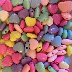 May include: A large assortment of heart-shaped beads in various pastel colors, including pink, blue, yellow, and purple. The beads are made of plastic and have a smooth, glossy finish.