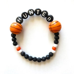 May include: A black and orange basketball themed bracelet with the name "HUNTER" spelled out in white letters on black beads.
