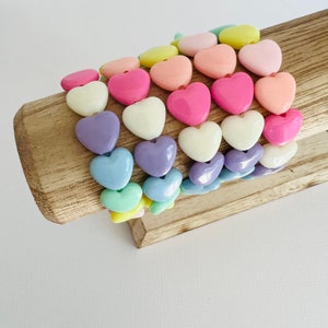 May include: A stack of colorful heart-shaped bracelets made of plastic beads. The bracelets are arranged in a rainbow pattern, starting with yellow and ending with purple.