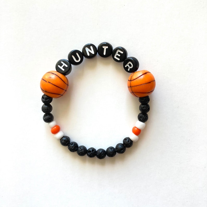 May include: Black and orange beaded bracelet with the name "HUNTER" spelled out in white letters. The bracelet also features two orange basketball-shaped beads.