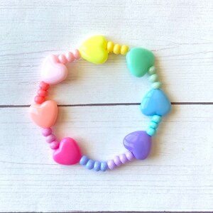 May include: A rainbow heart-shaped bead bracelet with pastel pink, orange, yellow, green, blue, and purple beads.