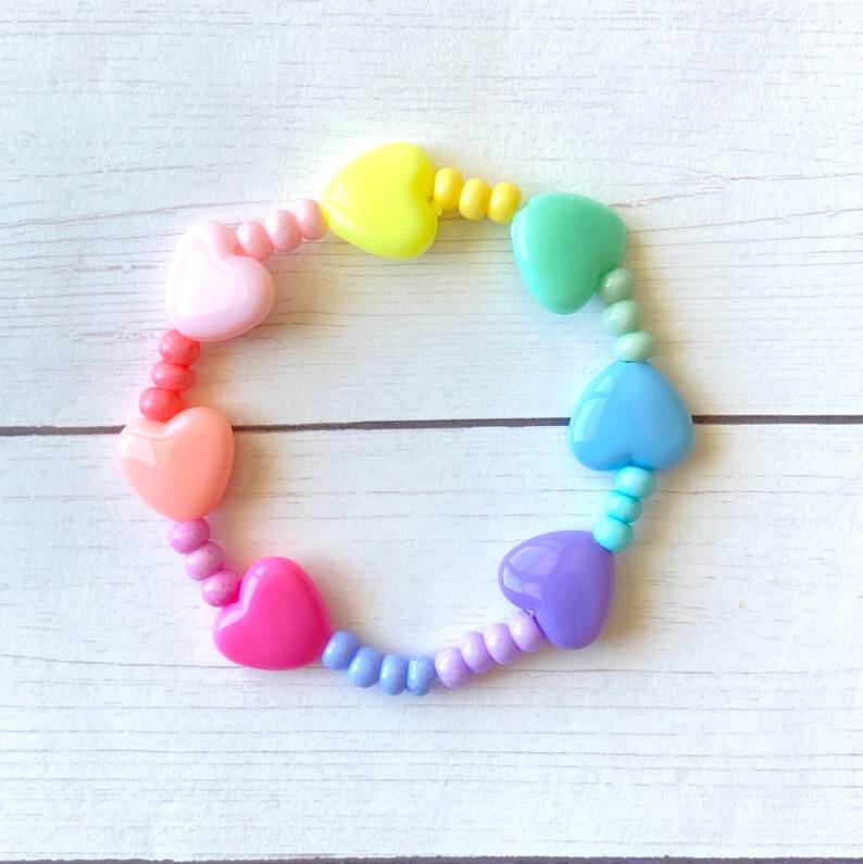 May include: A rainbow heart-shaped bead bracelet with pastel pink, orange, yellow, green, blue, and purple beads.