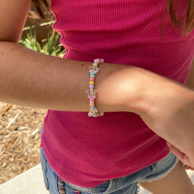May include: A colorful beaded bracelet with clear star-shaped charms. The beads are pastel pink, blue, yellow, and green.