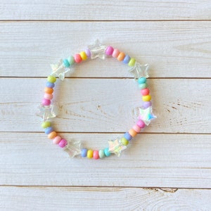 May include: A colorful beaded bracelet with iridescent star-shaped charms. The bracelet is made with pastel pink, yellow, blue, and green beads.