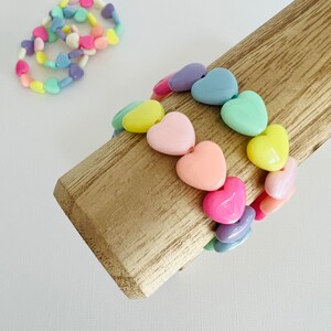 May include: A set of pastel-colored heart-shaped bracelets. The bracelets are made of plastic beads and are strung on elastic.