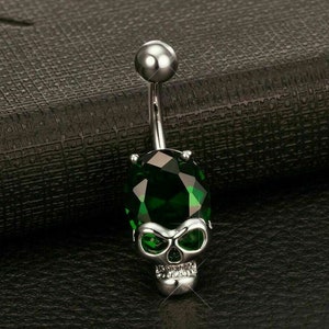 May include: A silver belly button ring with a green gem and a skull design.