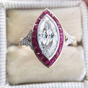 Può includere: Anello con diamante taglio marquise, con un'aureola di piccoli rubini quadrati. L'anello ha una fascia in oro con dettagli intricati e piccoli diamanti di accento sulle spalle. Lo stile è vintage o art déco.