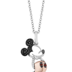 Puede incluir: Un collar de cadena de plata con un colgante de Mickey Mouse engastado con diamantes. El colgante presenta diamantes negros para las orejas y los ojos, y diamantes blancos para el contorno del cuerpo. El centro del cuerpo es de oro rosa.