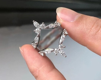 Puede incluir: Un anillo de plata con diseño cuadrado, adornado con múltiples piedras preciosas claras y brillantes. Las piedras están dispuestas en un patrón floral o de hojas alrededor de los bordes del anillo, creando una apariencia delicada y elegante.