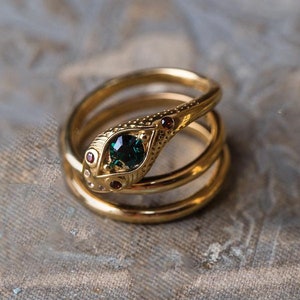 Peut inclure: Une bague en or avec un motif de serpent. La tête du serpent est ornée d'une pierre précieuse verte et de pierres précieuses rouges pour les yeux.