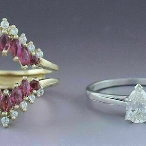 Puede incluir: Dos anillos de compromiso, uno con un diamante en forma de pera y el otro con un engaste de diamantes y rubíes. El anillo de rubí es un anillo de doble aro con un diseño de diamantes y rubíes.