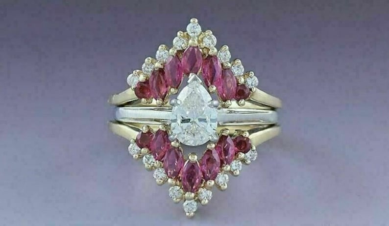 Puede incluir: Un anillo de compromiso de diamante de forma pera engastado con un halo de piedras preciosas de forma marquesa rosas. El anillo est&aacute; engastado en oro amarillo y tiene una banda de oro blanco.