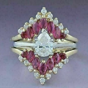 Puede incluir: Un anillo de compromiso de diamante de forma pera engastado con un halo de piedras preciosas de forma marquesa rosas. El anillo est&aacute; engastado en oro amarillo y tiene una banda de oro blanco.