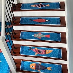Può includere: Un set di gradini per scale blu e bianchi con un design di pesci colorati. I gradini sono posizionati su una scala di legno con un runner rosso sul gradino superiore.