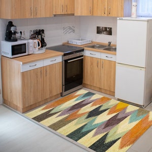 May include: A kitchen with wood cabinets and a white refrigerator. A colorful geometric rug is on the floor in front of the cabinets.