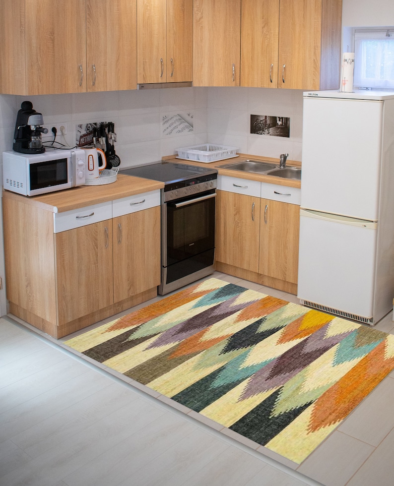 May include: A kitchen with wood cabinets and a white refrigerator. A colorful geometric rug is on the floor in front of the cabinets.