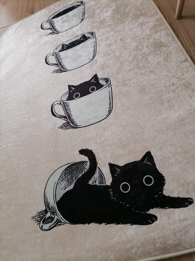 May include: A beige rug with a black cat illustration. The cat is depicted in various stages of entering a coffee cup. The cat is peeking out of the cup, then half-way in, and finally fully inside the cup.