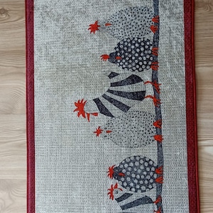 May include: A rectangular wall hanging with a repeating pattern of stylized chickens. The chickens are in black and white with red accents, arranged vertically on a light grey background. The border is a deep red.