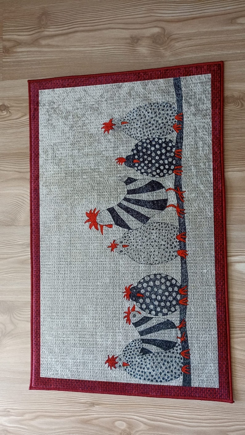 May include: A rectangular wall hanging with a repeating pattern of stylized chickens. The chickens are in black and white with red accents, arranged vertically on a light grey background. The border is a deep red.
