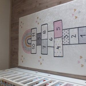 May include: A white rug with a hopscotch game printed on it. The hopscotch squares are pink, gray, and white with black outlines. The numbers 1 through 11 are printed in black on the squares. The rug is decorated with small pink and gold hearts.