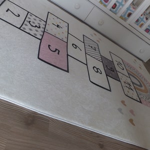 May include: A white play mat with a rainbow design and a hopscotch game printed on it. The hopscotch game features numbers 1 through 10 in black.