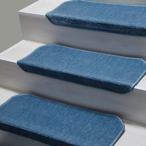 K&ouml;nnte beinhalten: Drei blaue Teppich-Treppenstufen mit einer strukturierten Oberfl&auml;che und einem hellblauen Rand. Die Stufen befinden sich auf einer wei&szlig;en Treppe.