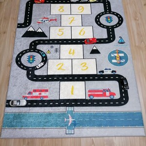 May include: A grey and blue play mat with a road and a runway for toy cars and aeroplanes. The mat features numbers 1 through 10, traffic lights, and a helicopter.