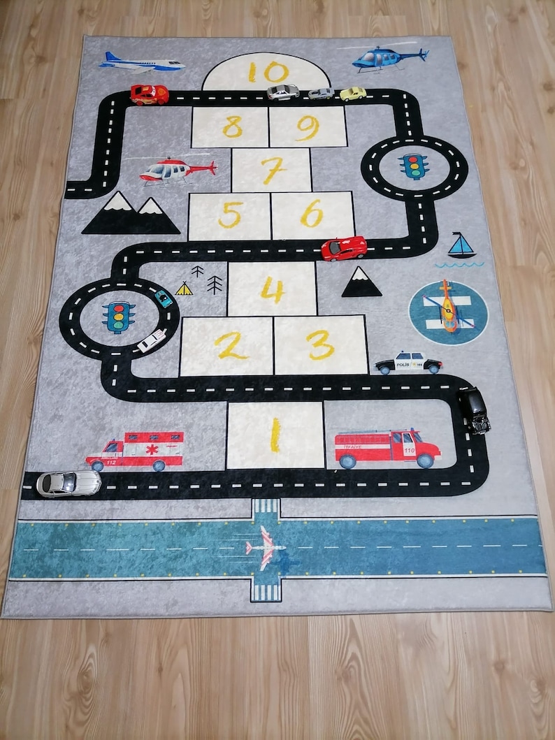 May include: A grey and blue play mat with a road and a runway for toy cars and aeroplanes. The mat features numbers 1 through 10, traffic lights, and a helicopter.