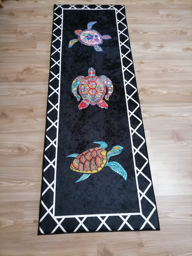 May include: A long, rectangular black rug with a white geometric border. The rug features three colorful sea turtle designs. The turtles have intricate patterns in shades of blue, red, yellow, and green.