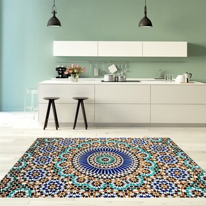 K&ouml;nnte beinhalten: Ein farbenfroher Teppich mit geometrischem Muster in einer K&uuml;che. Der Teppich hat einen zentralen blauen Kreis, der von t&uuml;rkisfarbenen, braunen und wei&szlig;en sternf&ouml;rmigen Formen umgeben ist. Die K&uuml;che hat wei&szlig;e Schr&auml;nke, schwarze Hocker und eine hellgr&uuml;ne Wand.
