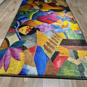 May include: Abstract rug with a colorful geometric design featuring a human figure playing a musical instrument. The rug has shades of blue, yellow, red, green, purple, and brown.