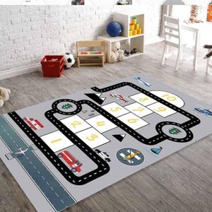 May include: A grey play mat with a black road and a hopscotch game with numbers 1-10. The mat features a fire engine, a police car, a helicopter, and an aeroplane.