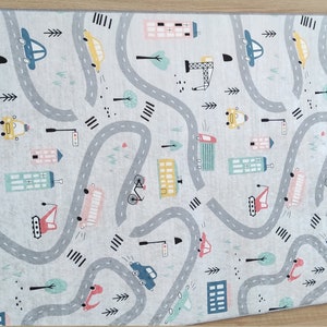 May include: A gray and white play mat with a city theme. The mat features a winding road with cars, trucks, and buildings. The road is surrounded by trees and streetlights.