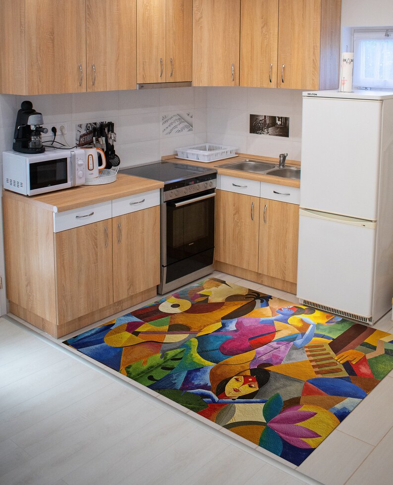 May include: A colorful abstract rug with a geometric design featuring a woman's face and a musical instrument. The rug is in a kitchen with white cabinets and a stainless steel oven.