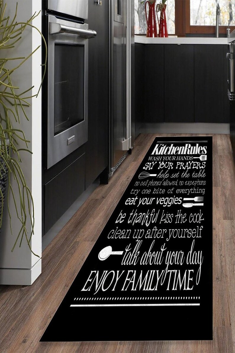 May include: Black and white kitchen rug with the text "Kitchen Rules" and a list of rules for family mealtime, including "Wash your hands", "Say your prayers", "Help set the table", "No cell phones allowed, no exceptions", "Try one bite of everything", "Eat your veggies", "Be thankful", "Kiss the cook", "Clean up after yourself", "Talk about your day", and "Enjoy family time".