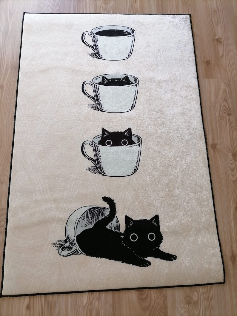 May include: A white rug with a black cat peeking out of a coffee cup. The cat is in three different stages of being in the cup, starting with just its head, then its head and shoulders, and finally the whole cat. The rug has a beige background.
