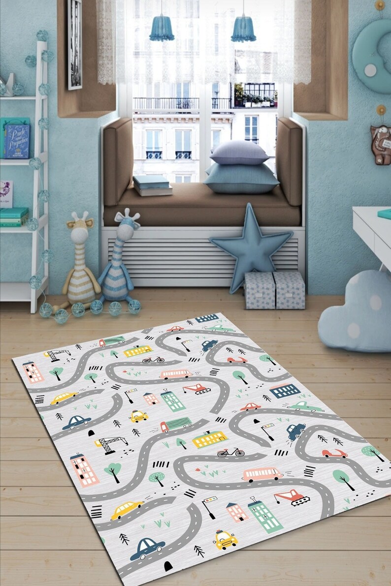 May include: A white play mat with a city road design featuring cars, buses, trucks, and buildings. The road is gray and the background is white with a light gray pattern.
