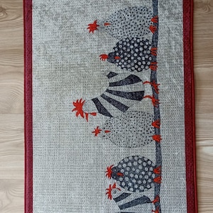 May include: A rectangular fabric wall hanging with a repeating pattern of stylized chickens. The chickens are in black and white with red accents, arranged on a vertical line against a light grey background. The border is a deep red.
