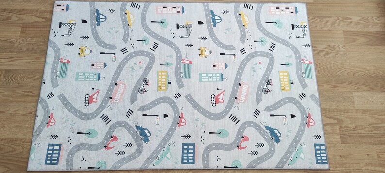 May include: A gray and white play mat with a city street design. The mat features winding roads, cars, trucks, bicycles, and buildings.