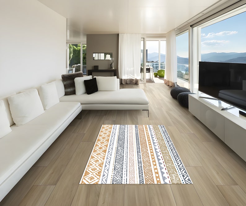 May include: A white sectional sofa with multiple pillows sits in a modern living room with large windows overlooking a mountain view. A patterned rug in shades of brown, gray, and white is on the floor in front of the sofa.