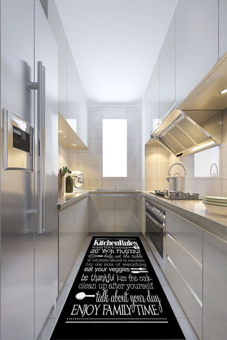 May include: Black and white kitchen rug with the text "Kitchen Rules" and a list of rules for the kitchen, including "Wash your hands", "Say your prayers", "Help set the table", "No cell phones allowed, no exceptions", "Try one bite of everything", "Eat your veggies", "Be thankful", "Kiss the cook", "Clean up after yourself", "Talk about your day", and "Enjoy family time".